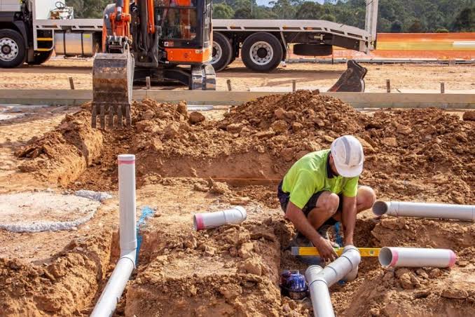 Worker installing pipework in an excavated site